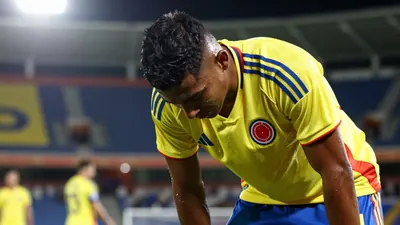 A young Colombian forward, mid-20s, athletic build, in Colombia's yellow and blue home kit with sharp crest, head bowed...