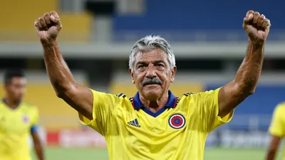 A 50-year-old Colombian coach with a weathered face, graying hair, and a thick mustache, stands on the Estadio...