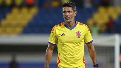 A tight, waist-up shot of a ruggedly-built, 35-year-old Colombian national team assistant coach, dressed in the Colombia...