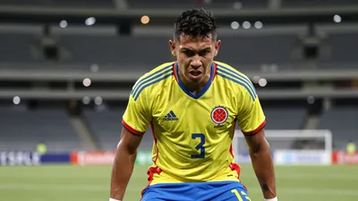 A close-up shot of a determined 28-year-old Colombian midfielder, dressed in the Colombia national team's home kit with a...