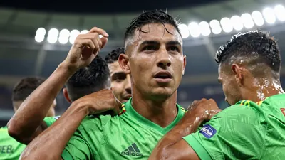 A Colombian national team player in a green jersey, celebrating with teammates after a goal