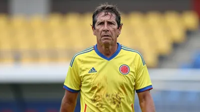 A tight, waist-up shot of a rugged, 35-year-old Colombian national team coach, his weathered face set in a determined...