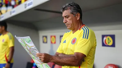 A medium shot of a rugged, 35-year-old Colombian national team assistant coach, with a weathered face and graying...
