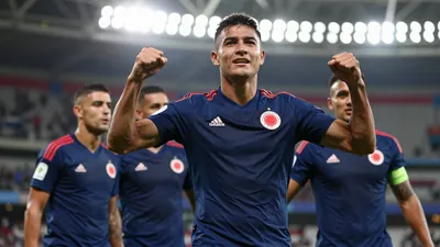 A 30-year-old Colombian national team player in a dark blue jersey, celebrating with teammates after a goal in a stadium