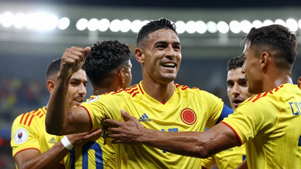A 30-year-old Colombian football player, wearing a yellow jersey, celebrating a goal with his teammates