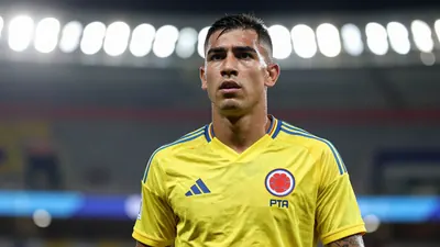 Mid-shot of a muscular 24-year-old Colombian defender, face sharp and expressive, wearing Colombia’s bright yellow and...