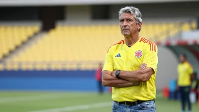 A 50-year-old Colombian coach, with a rugged complexion and graying hair, stands in front of a blurred Estadio...