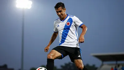 A 30-year-old, 5'9'' Colombian forward, wearing a white jersey with a blue stripe, a black short, and black socks, with a...