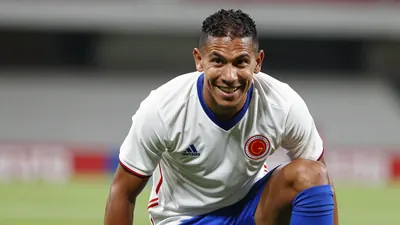 A photorealistic image of an anonymous Colombian player in a white jersey with blue shorts and blue socks, shot with a...